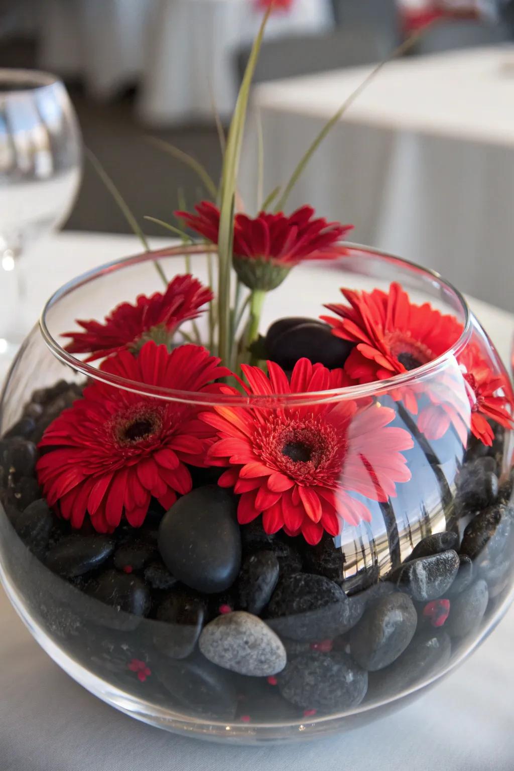 Drifting scarlet blossoms on ebony pebbles in a clear container for a serene centerpiece.