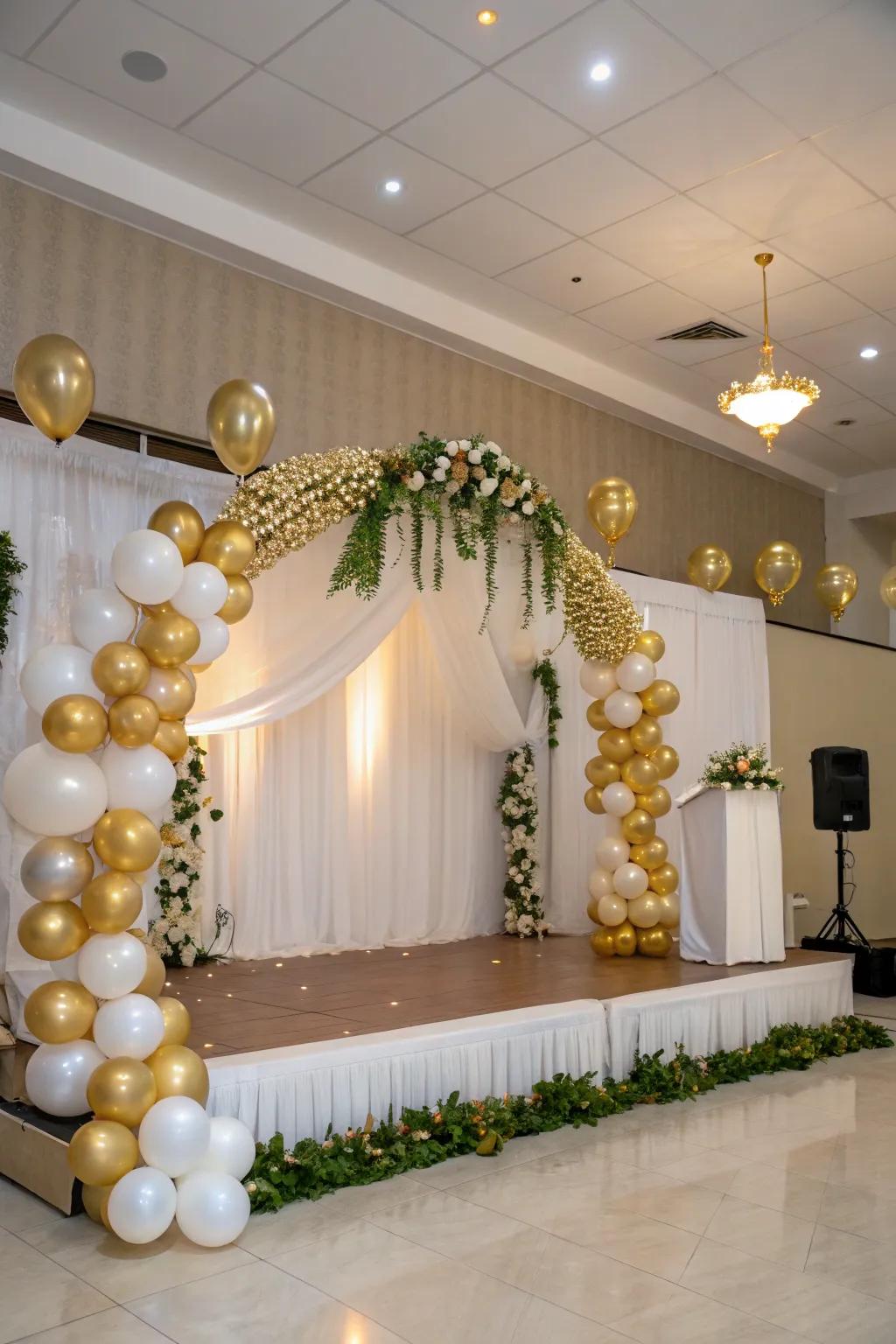 An elegant balloon arch and garland in gold and white framing the stage.