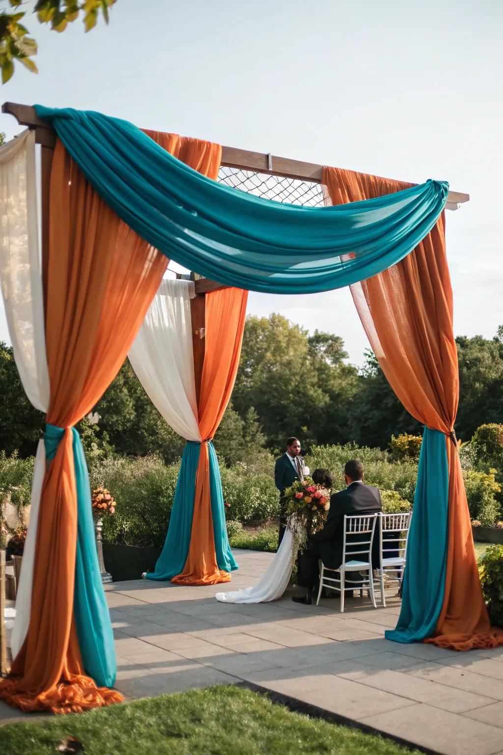 A ceremony arch draped in gorgeous aquatic blue and sunset fabrics.